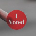 Person holding a red and white I voted sticker on their finger